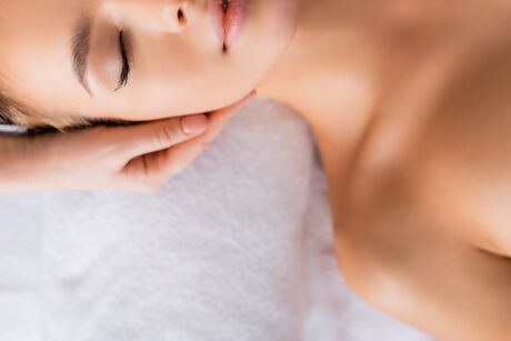 cropped view of masseur doing facial massage to young woman in spa salon